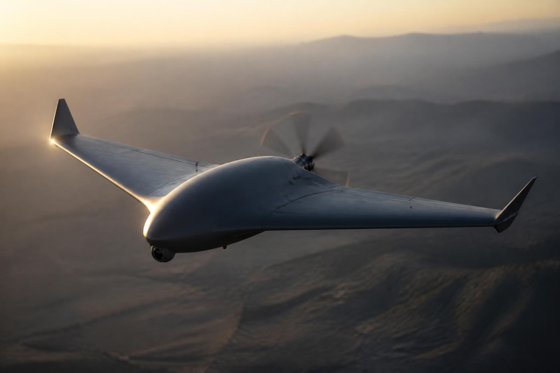 A tactical unmanned aerial vehicle in flight over a rugged coastline at dusk
