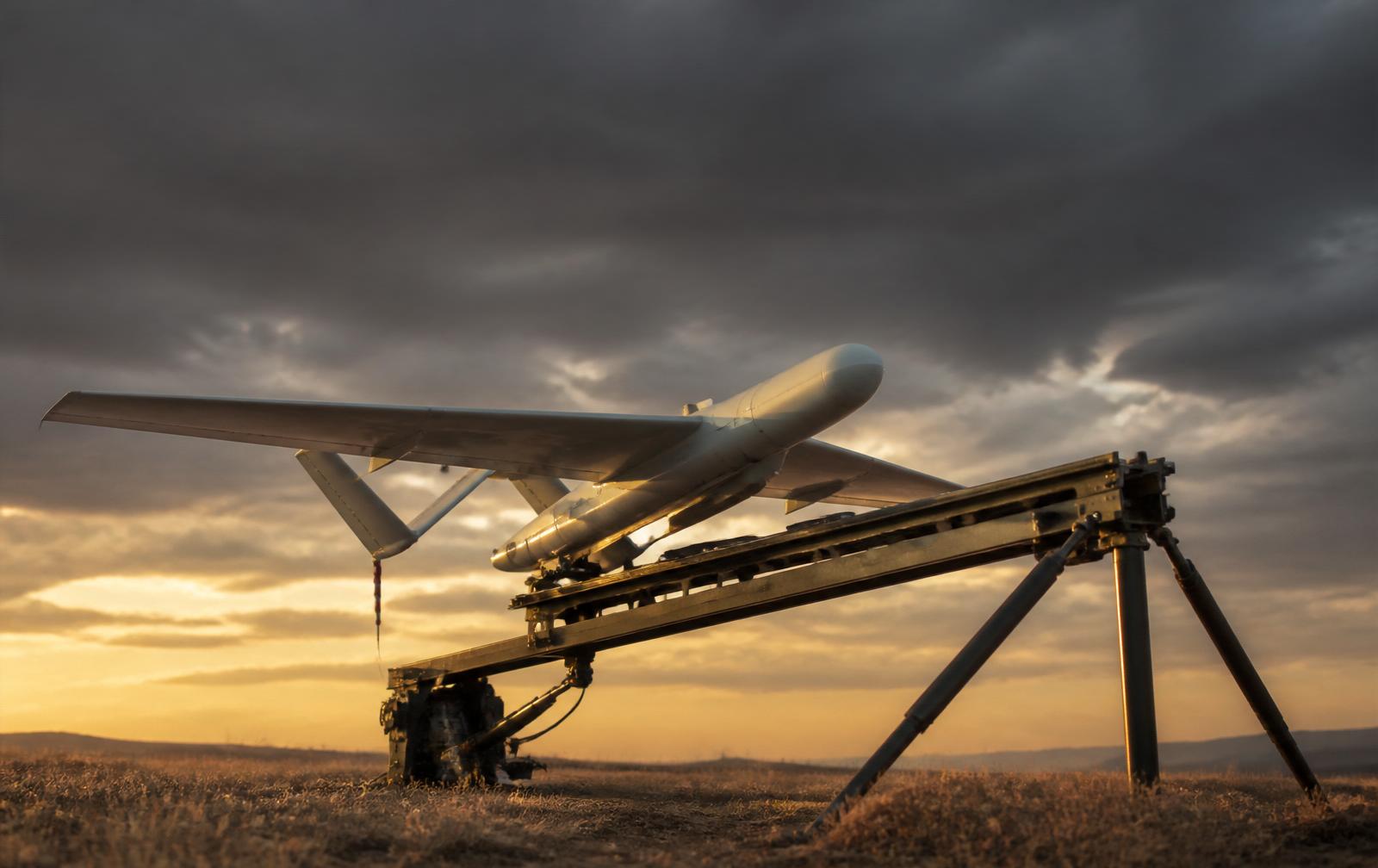 Fixed-wing interceptor drone on a pneumatic catapult launcher in a windswept field at dawn